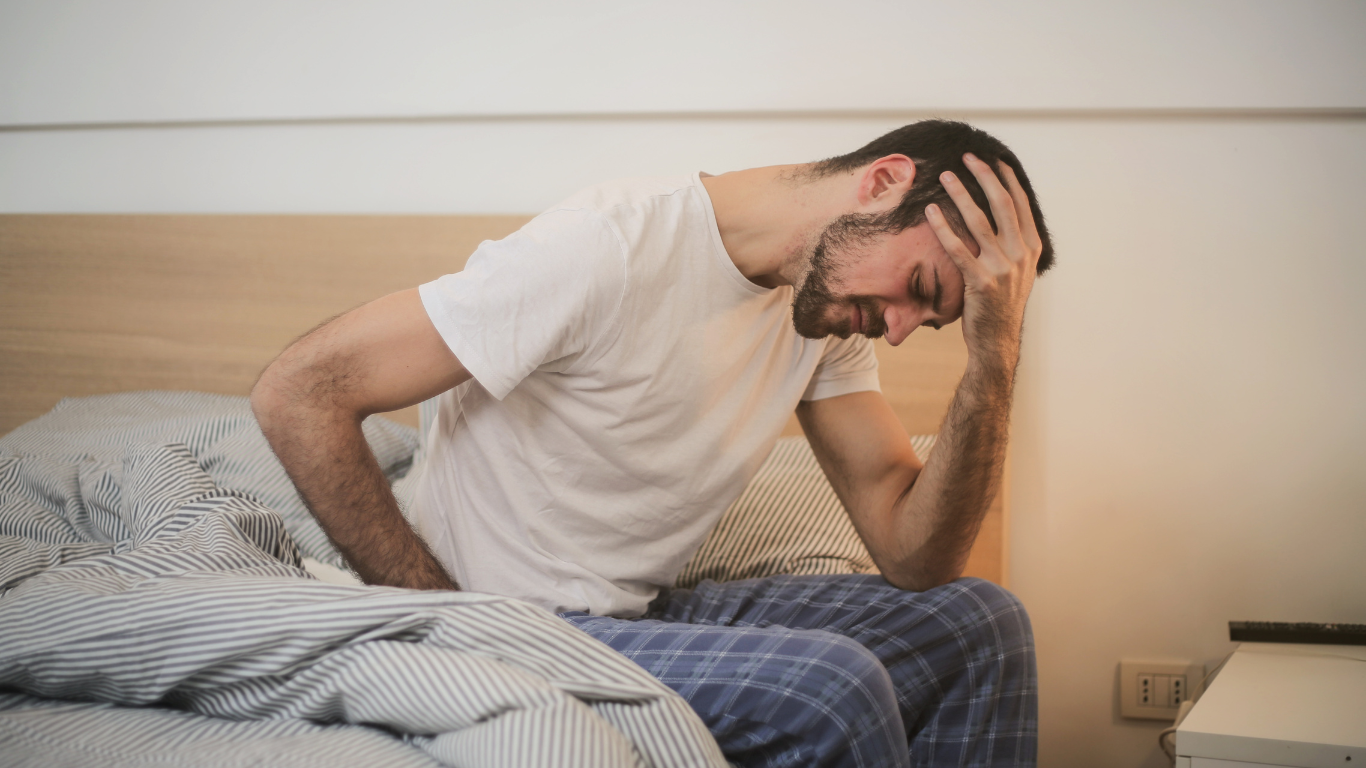 A man sitting on a bed holding his head