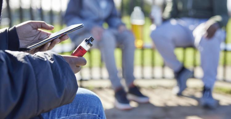 A youth sitting down looking at their phone while vaping