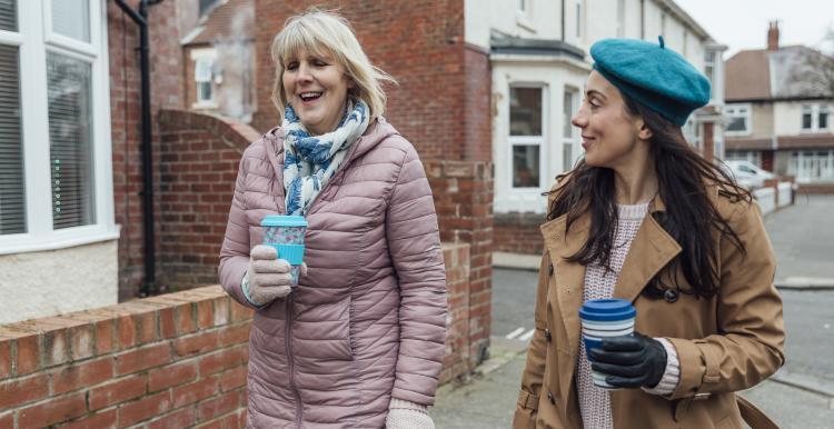 Two women walking down a street drinking coffee