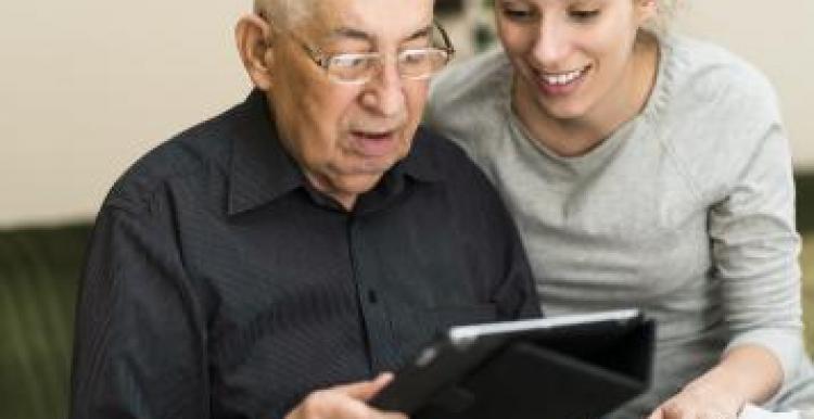 Young woman helping an elderly gentleman work a tablet