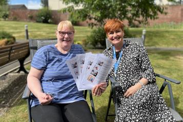 Two women sitting in a chair holding papers smiling at the camera